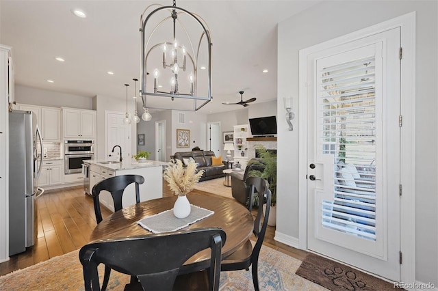 dining space featuring light wood finished floors, ceiling fan with notable chandelier, and recessed lighting