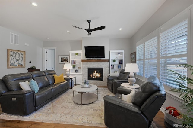 living area featuring recessed lighting, visible vents, a ceiling fan, wood finished floors, and a warm lit fireplace