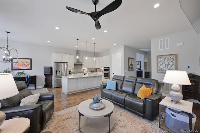 living area with ceiling fan with notable chandelier, recessed lighting, visible vents, and light wood-style floors