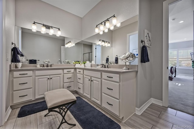 bathroom featuring baseboards, a sink, ensuite bath, and double vanity