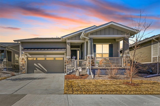 view of front facade featuring a porch, an attached garage, driveway, stone siding, and board and batten siding