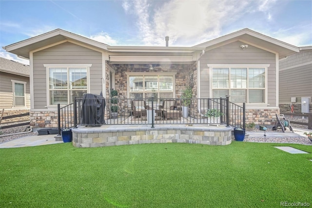 rear view of house featuring stone siding, a lawn, and a patio