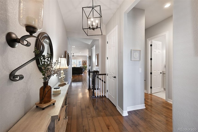 hall featuring dark wood-type flooring, an upstairs landing, and baseboards