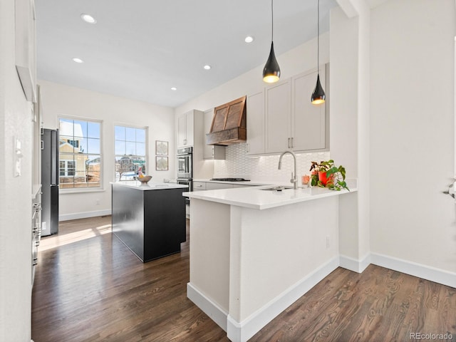 kitchen featuring decorative light fixtures, a peninsula, light countertops, premium range hood, and a sink