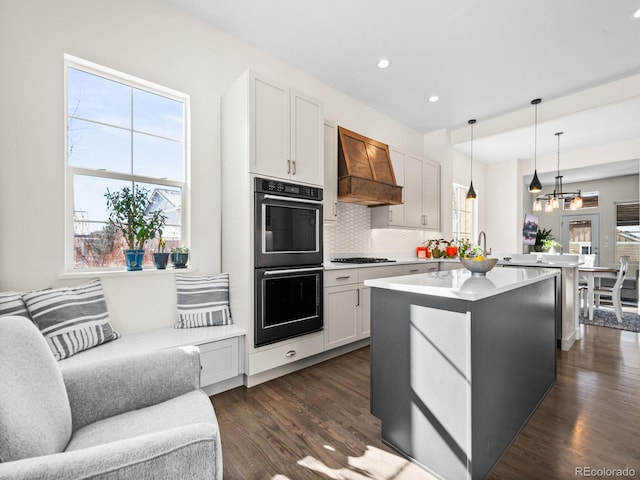 kitchen featuring stainless steel gas stovetop, white cabinetry, custom range hood, hanging light fixtures, and double oven