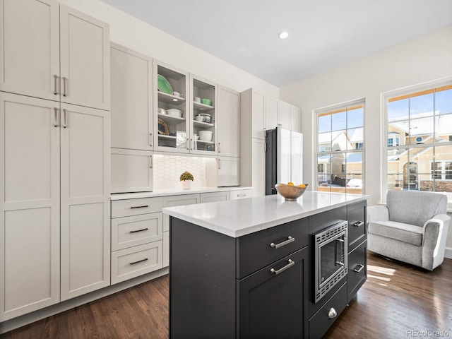 kitchen featuring dark wood-type flooring, a center island, stainless steel microwave, and white cabinetry