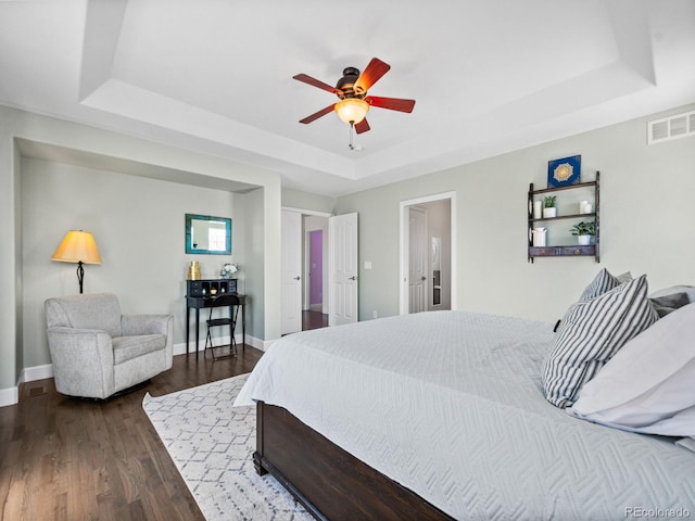 bedroom with dark hardwood / wood-style flooring, ceiling fan, and a raised ceiling