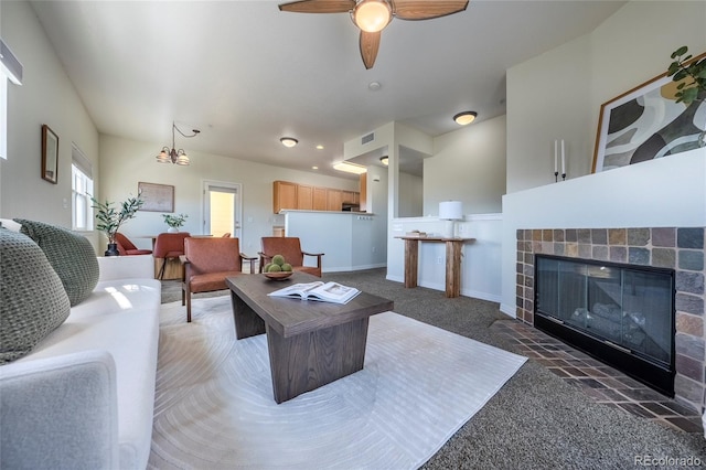 carpeted living room featuring ceiling fan with notable chandelier and a tile fireplace