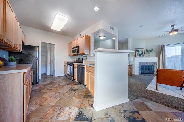 kitchen with ceiling fan, light brown cabinetry, appliances with stainless steel finishes, and a tile fireplace