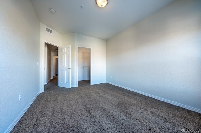 unfurnished bedroom with a walk in closet, a closet, and dark carpet