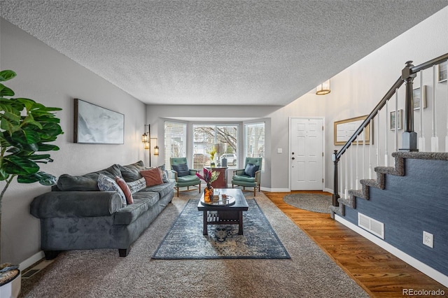 living room featuring visible vents, a textured ceiling, wood finished floors, baseboards, and stairs