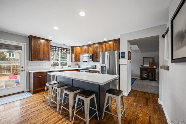 kitchen featuring tasteful backsplash, a kitchen island, appliances with stainless steel finishes, decorative light fixtures, and light countertops