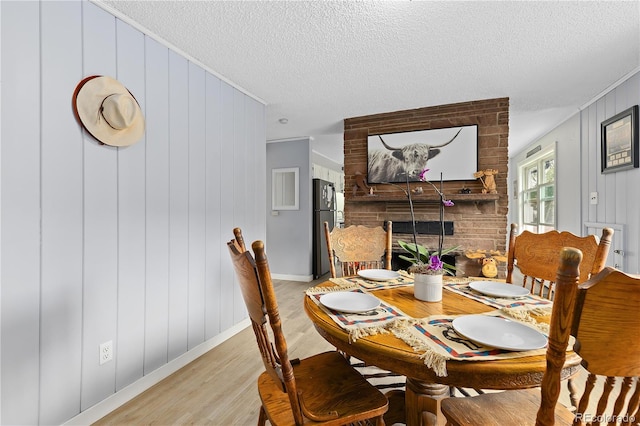 dining area with a fireplace, a textured ceiling, light wood-type flooring, and wood walls