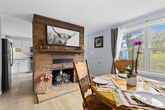 dining room featuring hardwood / wood-style floors, a textured ceiling, wooden walls, and a brick fireplace