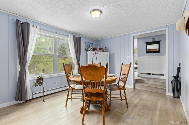 dining area with a textured ceiling, light wood-type flooring, and a baseboard radiator