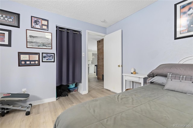 bedroom with light wood-style floors, a textured ceiling, and baseboards