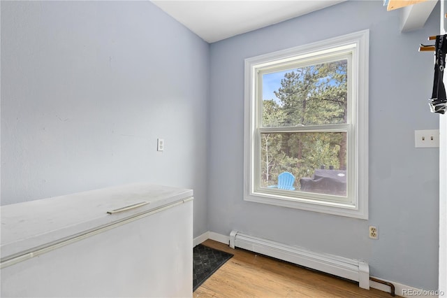 unfurnished room with a baseboard radiator, baseboards, and light wood-style flooring