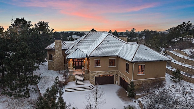 view of front of property with a chimney, stucco siding, an attached garage, stone siding, and driveway