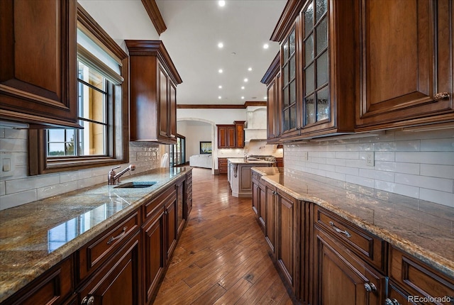 kitchen with arched walkways, glass insert cabinets, ornamental molding, a sink, and light stone countertops