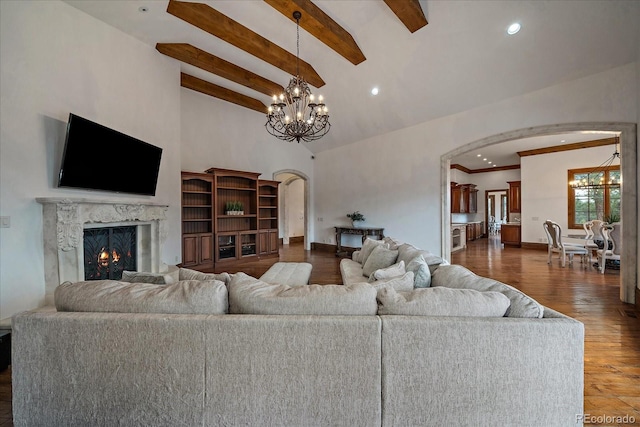 living room with arched walkways, a premium fireplace, dark wood-style flooring, beamed ceiling, and an inviting chandelier