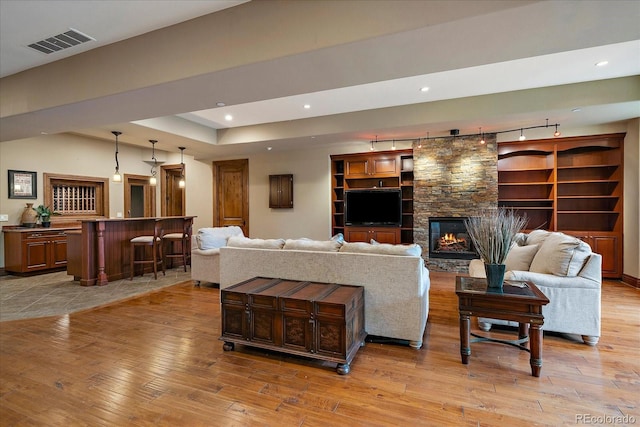 living room featuring recessed lighting, visible vents, a stone fireplace, and light wood finished floors