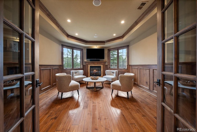 living area with wainscoting, a glass covered fireplace, visible vents, and wood-type flooring