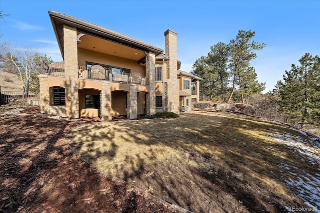 rear view of house featuring a yard, stucco siding, fence, a balcony, and stone siding