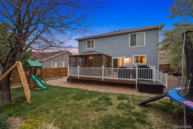 13818 Krameria St, Thornton, CO 80602 - back of house at dusk with a trampoline, a fenced backyard, a wooden deck, a lawn, and a playground
