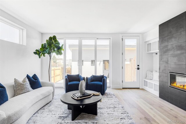 living area featuring wood finished floors, plenty of natural light, a tiled fireplace, and built in shelves