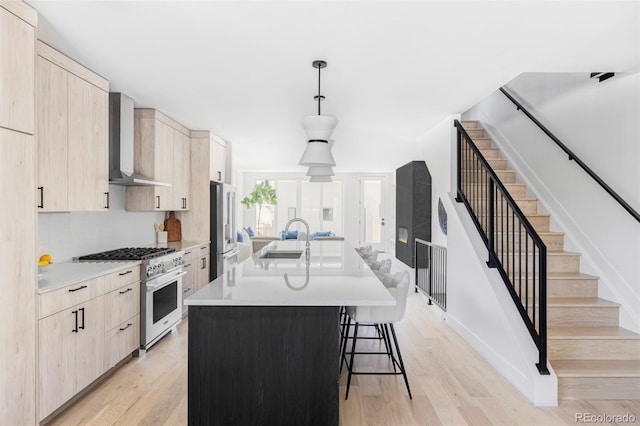 kitchen featuring gas range, light brown cabinets, wall chimney range hood, and stainless steel fridge
