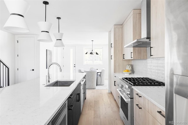 kitchen featuring appliances with stainless steel finishes, wall chimney exhaust hood, light brown cabinetry, a sink, and light wood-style floors