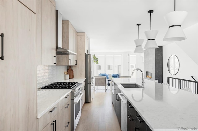 kitchen with stainless steel appliances, a sink, wall chimney exhaust hood, and light brown cabinets