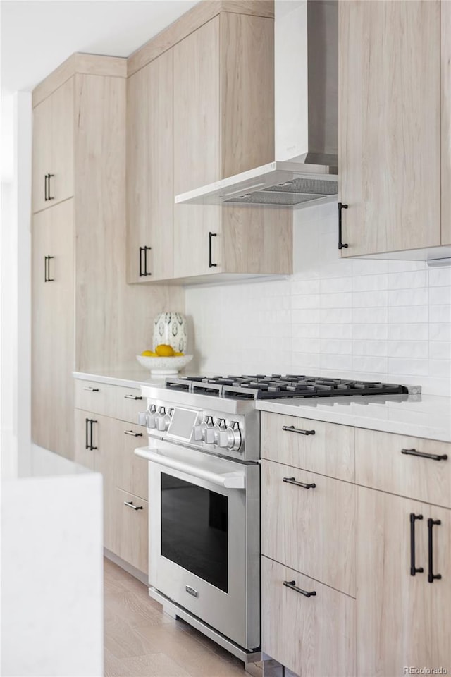 kitchen featuring light brown cabinets, stainless steel stove, wall chimney range hood, and modern cabinets
