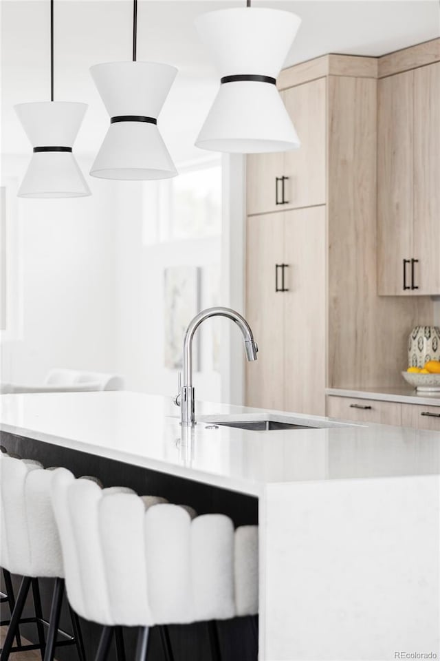 kitchen with light brown cabinetry, modern cabinets, light countertops, a breakfast bar, and a sink