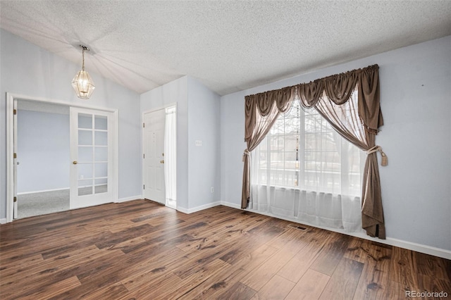 empty room featuring vaulted ceiling, dark wood-type flooring, french doors, and a textured ceiling