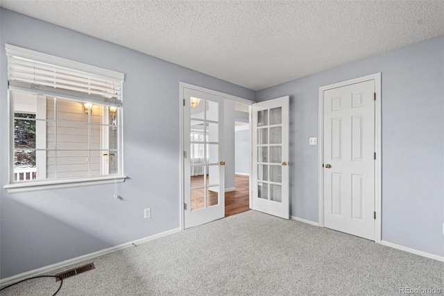 carpeted spare room featuring a textured ceiling and french doors