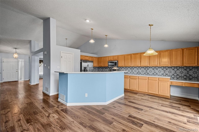 kitchen featuring pendant lighting, light hardwood / wood-style floors, a center island with sink, decorative backsplash, and appliances with stainless steel finishes