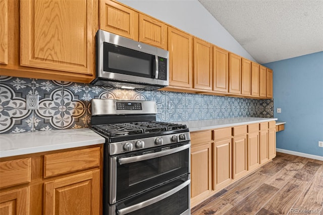 kitchen featuring vaulted ceiling, stainless steel appliances, light hardwood / wood-style floors, and backsplash