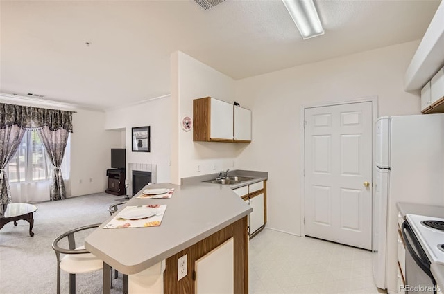 kitchen with a tiled fireplace, kitchen peninsula, sink, light colored carpet, and white cabinets