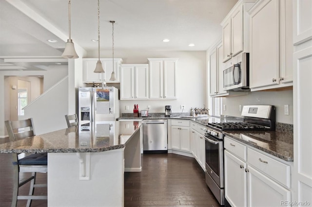 kitchen featuring dark stone counters, stainless steel appliances, white cabinets, a kitchen island, and a breakfast bar area