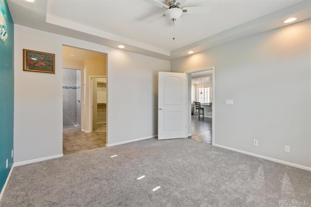 unfurnished bedroom featuring a tray ceiling, ceiling fan, carpet floors, and ensuite bathroom