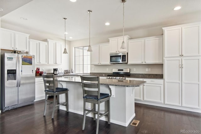 kitchen featuring appliances with stainless steel finishes, dark wood-type flooring, pendant lighting, a center island, and white cabinetry