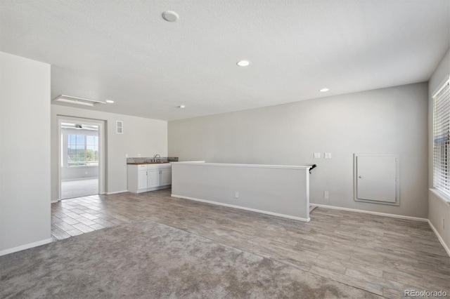 unfurnished living room featuring sink, light colored carpet, and a textured ceiling