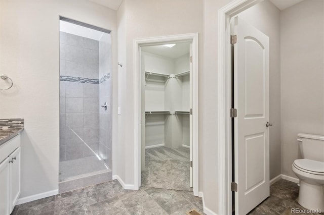 full bathroom with baseboards, tiled shower, toilet, a spacious closet, and vanity