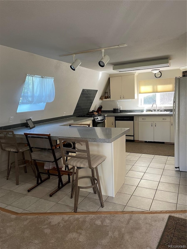 kitchen featuring a breakfast bar area, white cabinetry, stainless steel dishwasher, kitchen peninsula, and white fridge