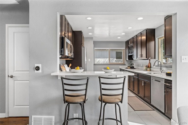 kitchen featuring a breakfast bar, appliances with stainless steel finishes, dark brown cabinetry, and a sink