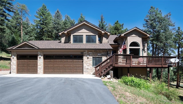 view of front facade with a wooden deck, an attached garage, a shingled roof, stone siding, and aphalt driveway