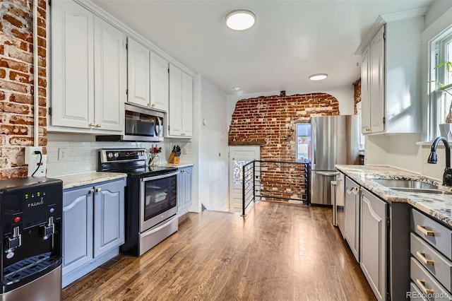 kitchen with appliances with stainless steel finishes, white cabinets, a sink, brick wall, and wood finished floors