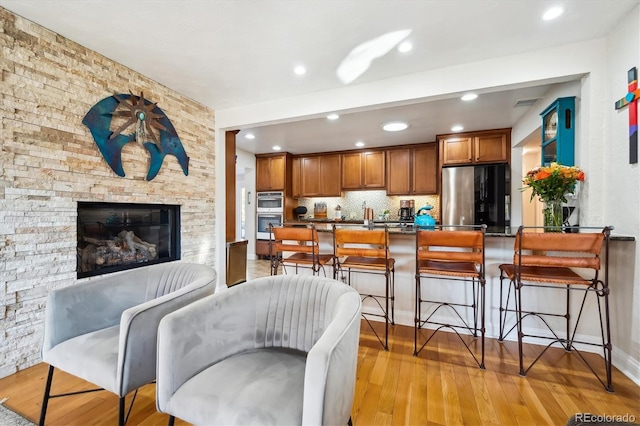 kitchen featuring light hardwood / wood-style floors, a kitchen bar, decorative backsplash, a fireplace, and appliances with stainless steel finishes