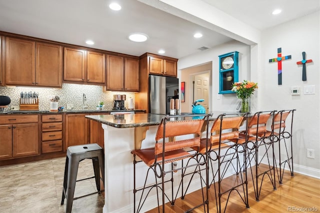 kitchen featuring stainless steel refrigerator with ice dispenser, light hardwood / wood-style flooring, a kitchen breakfast bar, and dark stone countertops